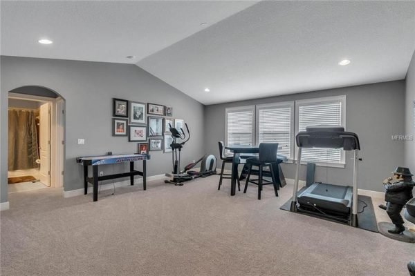 Spacious bonus room with exercise equipment, seating area, and large windows, showcasing a versatile living space in a Winter Garden home.