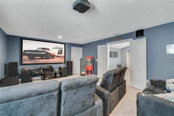 Home theater room featuring plush seating, large screen displaying "Fast and Furious 8," entertainment system, and popcorn machine, ideal for movie nights in a Winter Garden residence.