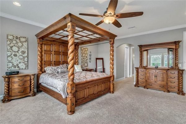 Master bedroom featuring a luxurious wooden four-poster bed, elegant furniture including a dresser and nightstand, plush carpet, and decorative wall art, highlighting spaciousness and comfort in a Winter Garden home.