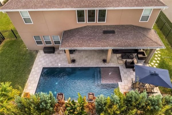 Aerial view of a modern home in Winter Garden, FL, featuring a saltwater heated pool, extensive decking, and covered lanai, surrounded by tropical landscaping in a gated community.