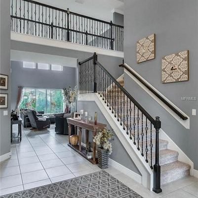 Spacious entryway of a modern home featuring a staircase with wrought iron railings, decorative wall art, and a view into a living area with large windows, highlighting the open floor plan and elegant design.
