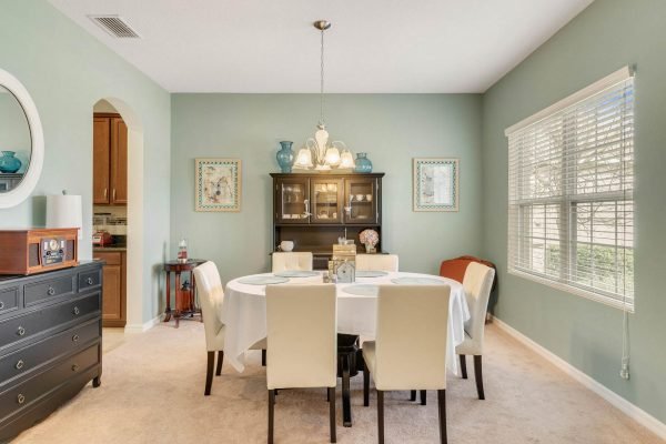 Dining room in 15522 Sandfield Loop, Winter Garden, FL, featuring a round table with white chairs, a dark wood sideboard, light green walls, and natural light from windows, showcasing a spacious and inviting atmosphere.