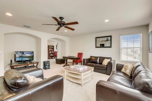 Spacious living room in a Taylor Morrison home, featuring leather sofas, a coffee table, and a television, with natural light from large windows and an open layout, ideal for entertaining.