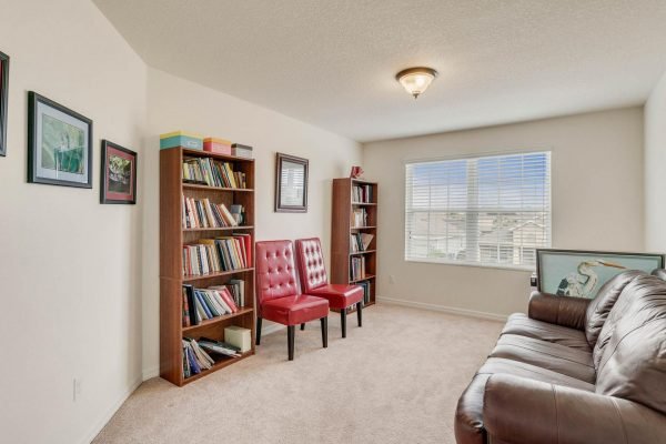 Cozy den with red chairs, bookshelf filled with books, and a window providing natural light, showcasing the inviting interior of 15522 Sandfield Loop, Winter Garden, FL.