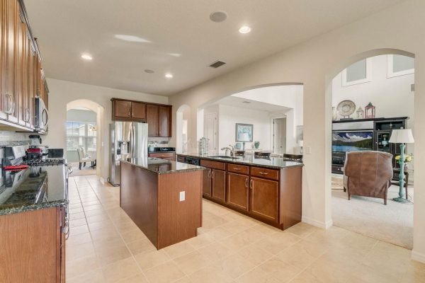 Modern kitchen with dark wood cabinetry, granite countertops, and stainless steel appliances, featuring an open layout leading to a spacious living area in a home located at 15522 Sandfield Loop, Winter Garden, FL.