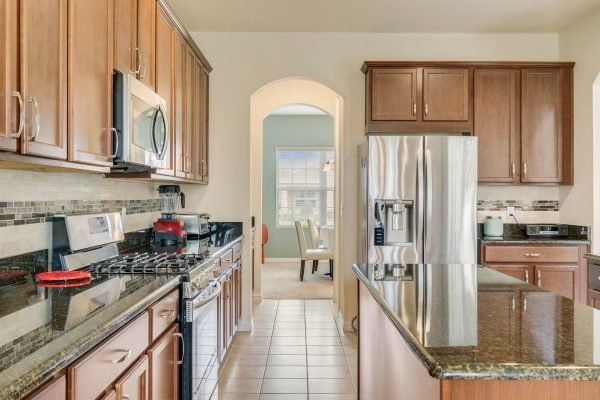 Modern kitchen with dark wood cabinetry, stainless steel appliances, granite countertops, and a view into a dining area, highlighting the spacious layout of the home at 15522 Sandfield Loop, Winter Garden, FL.