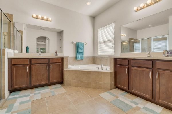 Spacious master bathroom with dual vanities, large soaking tub, and natural light, featuring modern fixtures and tile flooring, located in a home for sale at 15522 Sandfield Loop, Winter Garden, FL.