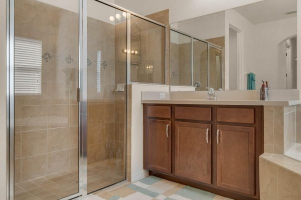 Master bathroom featuring a spacious shower with glass enclosure, dual sink vanity with wooden cabinetry, and neutral tile flooring, located in a well-maintained home at 15522 Sandfield Loop, Winter Garden, FL.