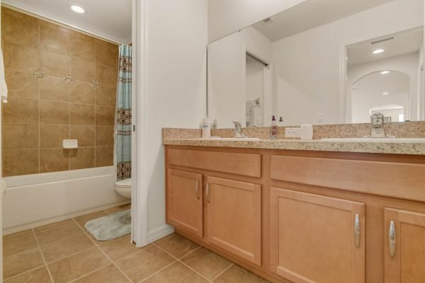 Bathroom interior featuring a double vanity with wooden cabinetry, granite countertops, and a bathtub with a tiled shower area, showcasing a clean and modern design in a home for sale at 15522 Sandfield Loop, Winter Garden, FL.