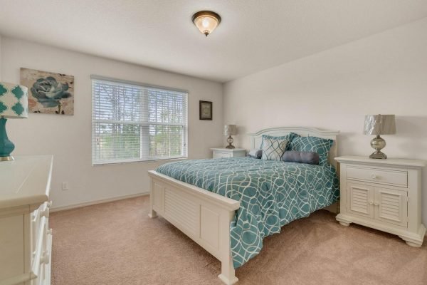 Bright bedroom featuring a queen-sized bed with teal and white bedding, two nightstands with lamps, and a large window allowing natural light, situated in the well-maintained home at 15522 Sandfield Loop, Winter Garden, FL.