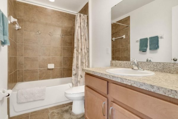 Bathroom with tiled walls, bathtub with shower curtain, and granite countertop, featuring a sink and wooden cabinetry, located in a home for sale at 15522 Sandfield Loop, Winter Garden, FL.