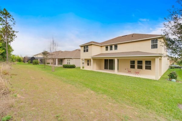 Backyard view of 15522 Sandfield Loop, Winter Garden, FL, featuring a spacious lawn, neighboring homes, and a clear blue sky, highlighting the property's outdoor living potential in a gated community.