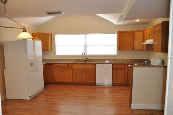 Kitchen interior at 1006 Venetian Ave, Orlando, featuring wooden cabinets, granite countertops, stainless steel dishwasher, and large windows providing natural light.