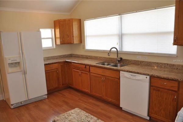 Modern kitchen with wooden cabinets, granite countertops, stainless steel refrigerator, and dishwasher, featuring large windows for natural light, located at 1006 Venetian Ave, Orlando, FL.