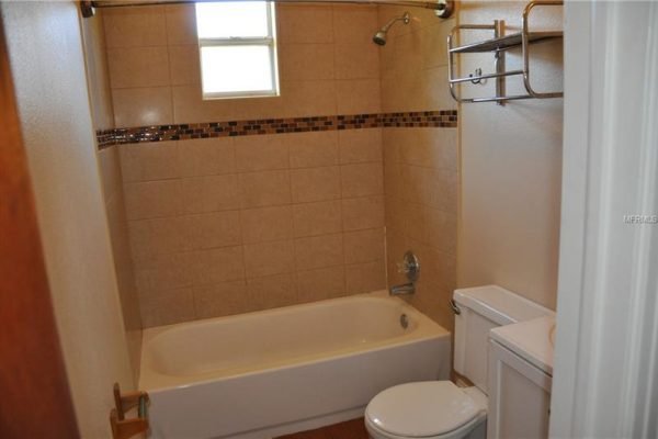 Bathroom featuring a tub and shower combination with tiled walls, beige color scheme, and a window for natural light, located in a 3-bedroom home for sale at 1006 Venetian Ave, Orlando, FL.