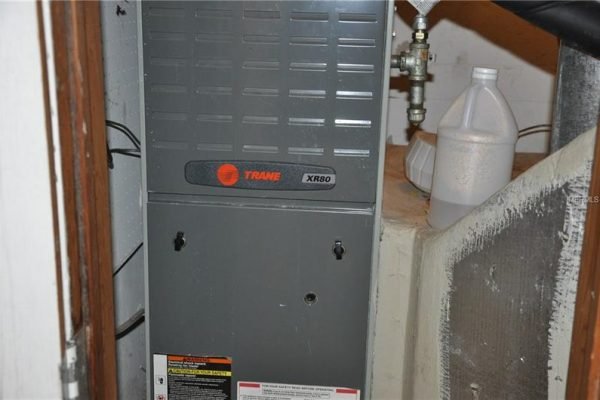 Trane XR80 heating system installed in a residential setting, showcasing a gray furnace unit with visible labels and a nearby water container.