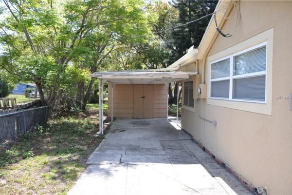 Carport and side view of the home at 1006 Venetian Ave, surrounded by mature trees, showcasing a partially fenced yard in University Heights, Orlando, FL.