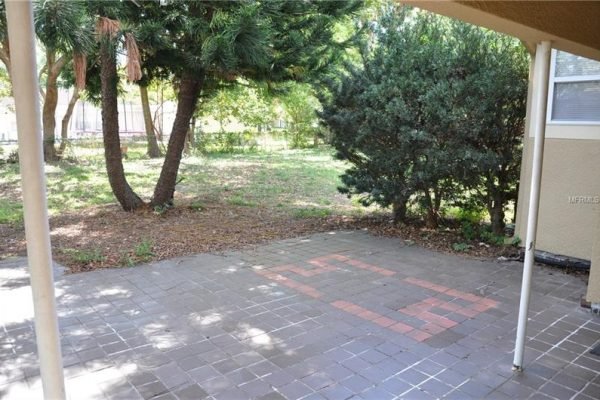 Patio area with tile flooring and landscaped yard featuring mature trees at 1006 Venetian Ave, Orlando, FL, highlighting outdoor space for potential buyers.