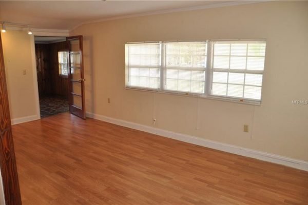 Interior view of a living room in a home at 1006 Venetian Ave, Orlando, featuring hardwood floors, large windows providing natural light, and a doorway leading to another room.