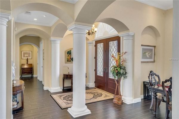 Elegant entryway of a luxury home at 11114 Romance Ct, Winter Garden, featuring arched columns, double front doors with glass panels, decorative plants, and a stylish rug, showcasing the home's sophisticated design and open concept layout.