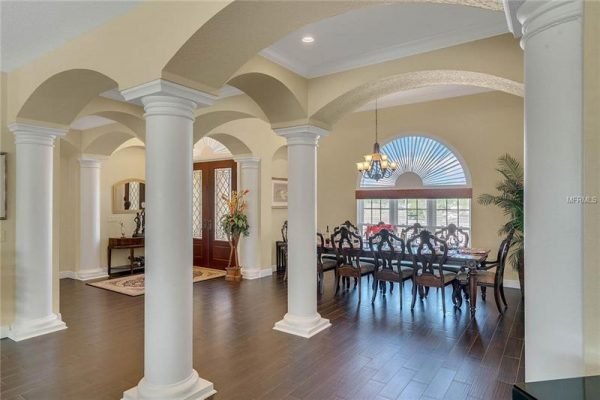 Elegant entryway of a luxury home featuring decorative columns, a spacious dining area with a chandelier, and large windows allowing natural light, showcasing the refined interior design of the property at 11114 Romance Ct, Winter Garden, FL.