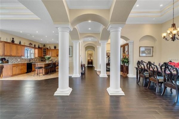 Elegant interior view of 11114 Romance Ct in Winter Garden, showcasing open concept design with polished dark wood floors, decorative columns, and a spacious kitchen with wooden cabinetry, emphasizing luxury and sophistication in real estate.