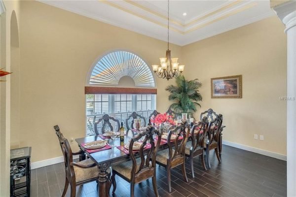 Elegant dining room at 11114 Romance Ct in Winter Garden, featuring a large wooden table set for dining, ornate chairs, decorative chandelier, and large window with arch design, showcasing a sophisticated interior design.