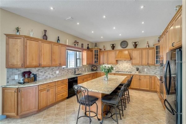 Spacious kitchen with wooden cabinetry, granite countertops, and modern appliances, featuring a large island and decorative accents, showcasing elegance and functionality in a luxury home in Winter Garden, FL.