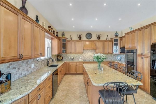 Spacious kitchen featuring wooden cabinetry, granite countertops, modern appliances, and decorative accents, highlighting elegance and functionality in the property at 11114 Romance Ct, Winter Garden, FL.