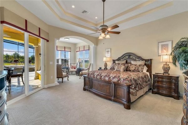 Spacious master bedroom with elegant wooden bed, decorative bedding, and large windows showcasing outdoor views, emphasizing luxury living at 11114 Romance Ct, Winter Garden, FL.