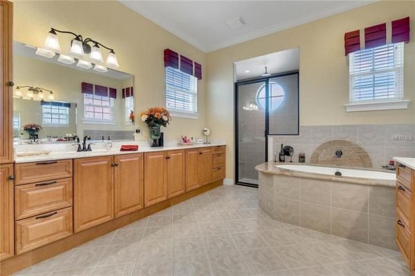 Elegant bathroom featuring wooden cabinetry, dual sinks, a soaking tub, and a glass-enclosed shower, with natural light from multiple windows and decorative accents.