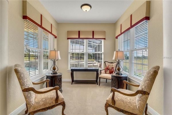 Bright sunroom with two elegant chairs, side tables, and lamps, featuring large windows with blinds, offering scenic views, in the luxury home at 11114 Romance Ct, Winter Garden, FL.