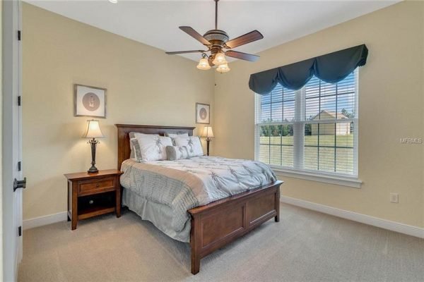 Cozy bedroom featuring a wooden bed frame with decorative pillows, bedside tables with lamps, and large windows allowing natural light, located in a luxurious home at 11114 Romance Ct, Winter Garden, FL.