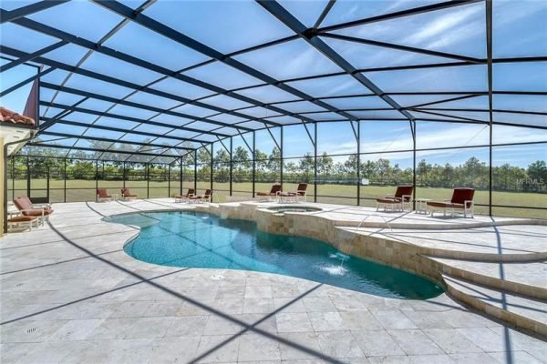 Resort-style pool area with screened enclosure, surrounded by lounge chairs and lush greenery, showcasing the luxurious outdoor living space at 11114 Romance Ct, Winter Garden, FL.