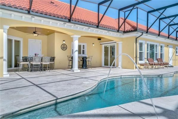 Backyard view of luxury home at 11114 Romance Ct in Winter Garden, FL, featuring a sparkling pool, outdoor dining area with table and chairs, and covered lanai under a screened enclosure, showcasing elegant design and resort-style amenities.