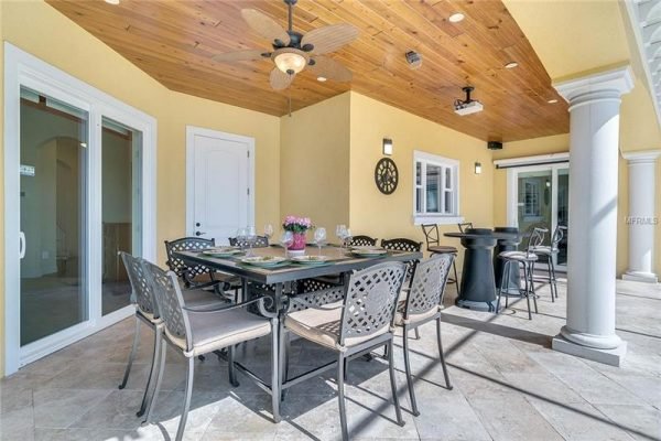 Outdoor dining area featuring a table with chairs, elegant ceiling fan, and decorative wall clock, showcasing the luxurious patio of a home at 11114 Romance Ct in Winter Garden, FL.