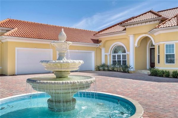 Elegant fountain in front of a luxurious home at 11114 Romance Ct, Winter Garden, FL, featuring a paver driveway and vibrant landscaping, highlighting the property's upscale curb appeal.