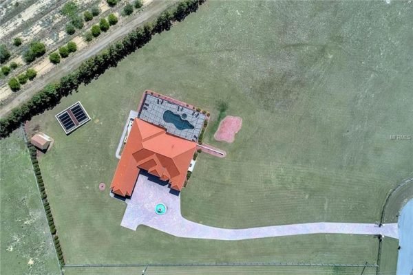 Aerial view of a luxurious home at 11114 Romance Ct in Winter Garden, FL, showcasing a spacious layout, resort-style pool, extensive travertine deck, and a vast green yard on a fully fenced 4-acre property.