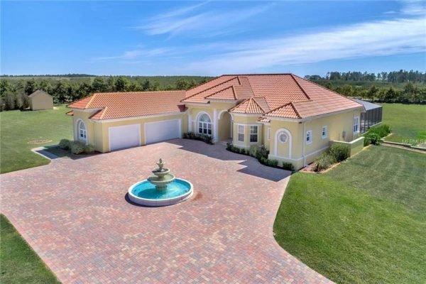 Elegant home at 11114 Romance Ct in Winter Garden, FL, featuring a stunning fountain, spacious brick paver driveway, and lush green surroundings on a 4-acre lot.