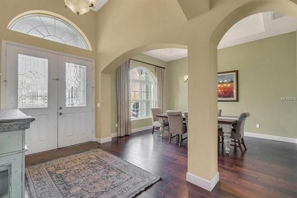 Spacious entryway of a luxurious home at 11630 Flynn Ct, Winter Garden, featuring double doors, arched windows, hardwood flooring, and a dining area with elegant furnishings.