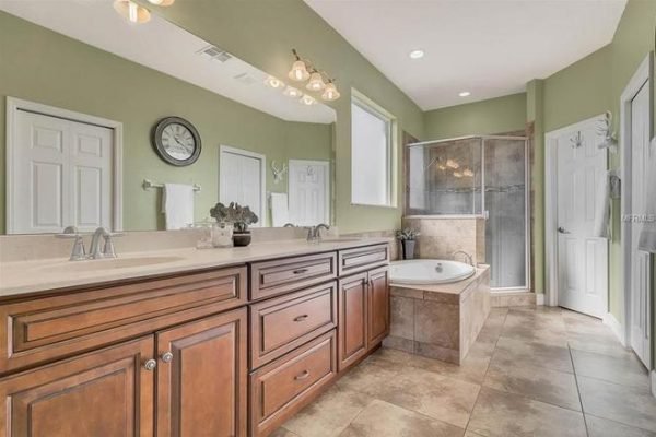 Spacious bathroom with dual sinks, wooden cabinetry, large soaking tub, and walk-in shower, featuring green walls and natural light from windows, ideal for the Winter Garden property at 11630 Flynn Ct.