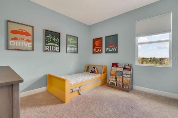 Children's bedroom featuring a yellow bed with playful decor, framed motivational posters on the walls, and a bookshelf filled with children's books, highlighting a bright and inviting atmosphere.