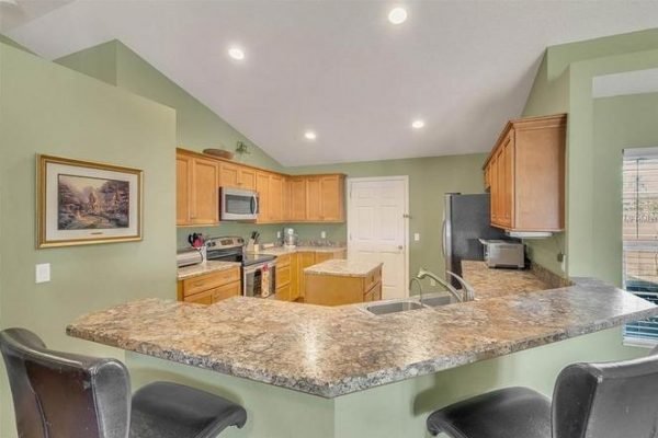 Modern kitchen with granite countertops, wooden cabinetry, stainless steel appliances, and a bar seating area, showcasing the interior of the property at 11630 Flynn Ct, Winter Garden, FL.