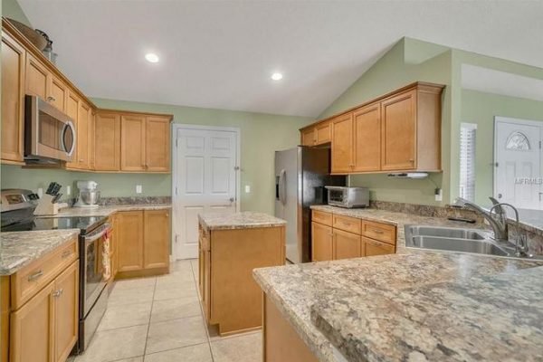 Modern kitchen with wooden cabinetry, granite countertops, stainless steel appliances, and tile flooring in a spacious layout at 11630 Flynn Ct, Winter Garden, FL.