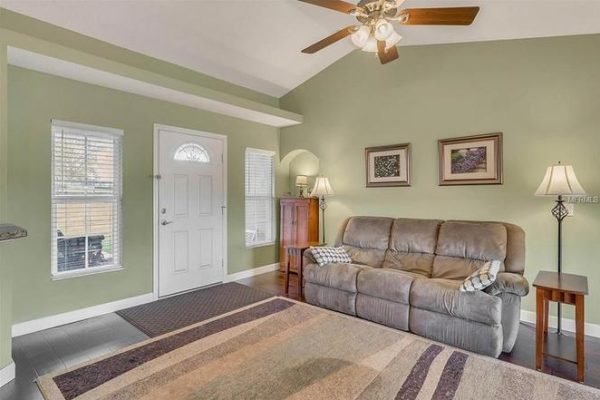 Cozy living room in Winter Garden, FL home featuring a comfortable sofa, decorative artwork, and natural light from windows, ideal for showcasing the inviting interior of the property at 11630 Flynn Ct.