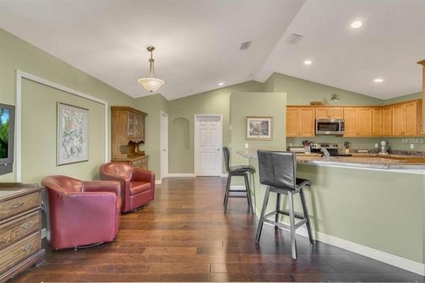 Spacious living area in Winter Garden home featuring hardwood floors, kitchen with wooden cabinetry, and seating area with red accent chairs.