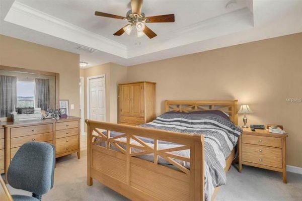 Cozy bedroom with wooden furniture, ceiling fan, and large window, showcasing a comfortable ambiance in the home at 11630 Flynn Ct, Winter Garden, FL.