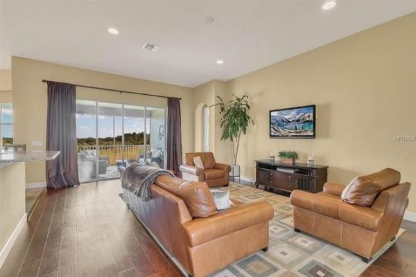 Spacious living room in Winter Garden estate featuring leather sofas, large windows with views, and a mounted TV, highlighting the inviting interior of the property at 11630 Flynn Ct.