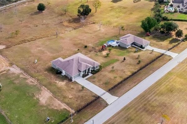 Aerial view of a spacious 5-acre estate in Winter Garden, FL, featuring two single-family homes, lush green lawn, above-ground saltwater pool, and ample outdoor space.