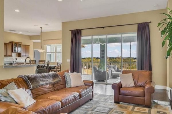Spacious living room in Winter Garden estate featuring leather sofas, large windows with scenic views, and an open kitchen layout, highlighting the inviting atmosphere of the property at 11630 Flynn Ct.